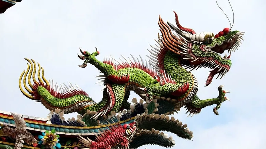 Una escultura de un dragón chino en el techo de un templo rodeado de otras esculturas coloridas de aves y flores. El dragón es verde con acentos rojos y amarillos. Esta imagen está relacionada con la mitología y los mitos